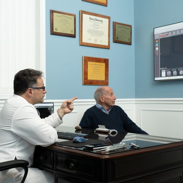 In an office adorned with certificates, a doctor from Three Village Neurology attentively explains a brain scan on the screen to an older man, highlighting the importance of dedicated neurological care. In an office adorned with certificates, a doctor from Three Village Neurology attentively explains a brain scan on the screen to an older man, highlighting the importance of dedicated neurological care.