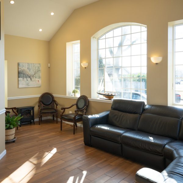 A sunny living room with a black leather sectional sofa, two wooden chairs, potted plants, and large windows evokes the calm expertise of a Neurology Specialist's office at Three Village Neurology. A sunny living room with a black leather sectional sofa, two wooden chairs, potted plants, and large windows evokes the calm expertise of a Neurology Specialist's office at Three Village Neurology.